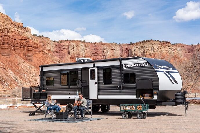 Toy hauler campground with a couple sitting outside, red cliffs in the background