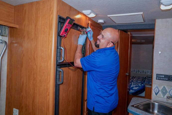 Technician troubleshooting RV refrigerator using a multimeter