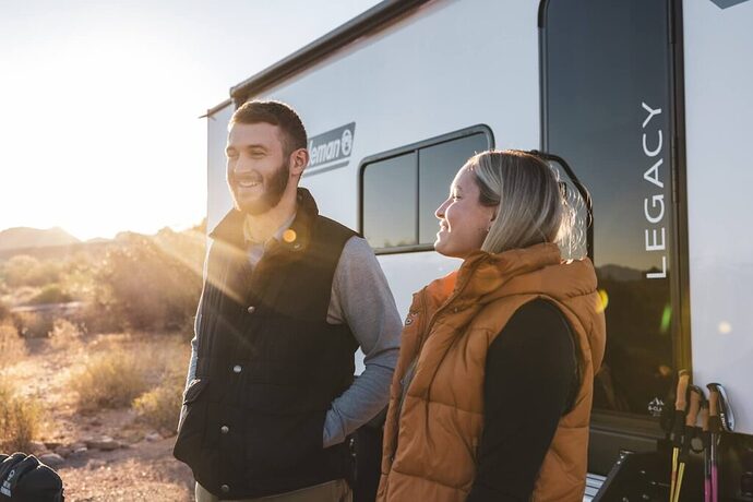 Two campers standing in front of their Coleman travel trailer. 