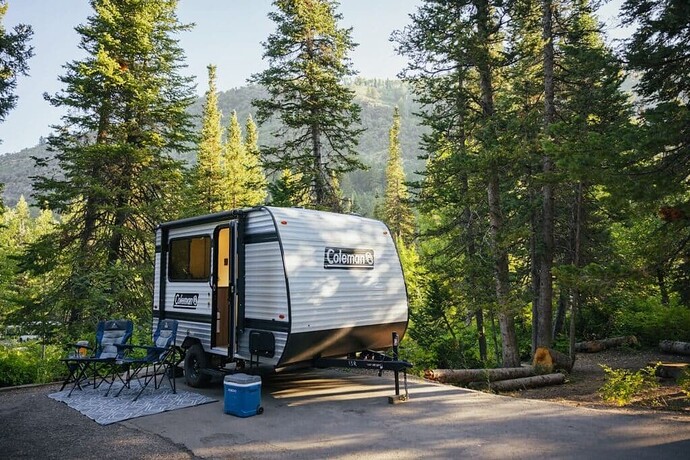 Small RV at a campsite with woods and mountains in the background