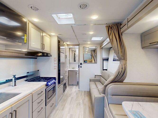 Interior image of the living area for the Thor Coleman 24CL RV. The left of the image features a galley kitchen and the right features part of the dinette and the sofa. 