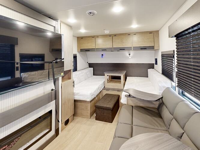 Image of the interior of the Campsite Reserve 20AJ facing the front of the RV. It includes a TV to the left, sofa to the right and covertible dining area straight ahead.